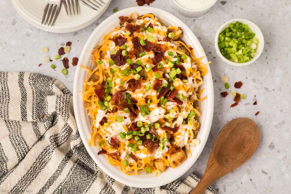 Loaded Tater Tots on a white platter topped with shredded cheese, ranch dressing, chopped bacon and sliced green onions