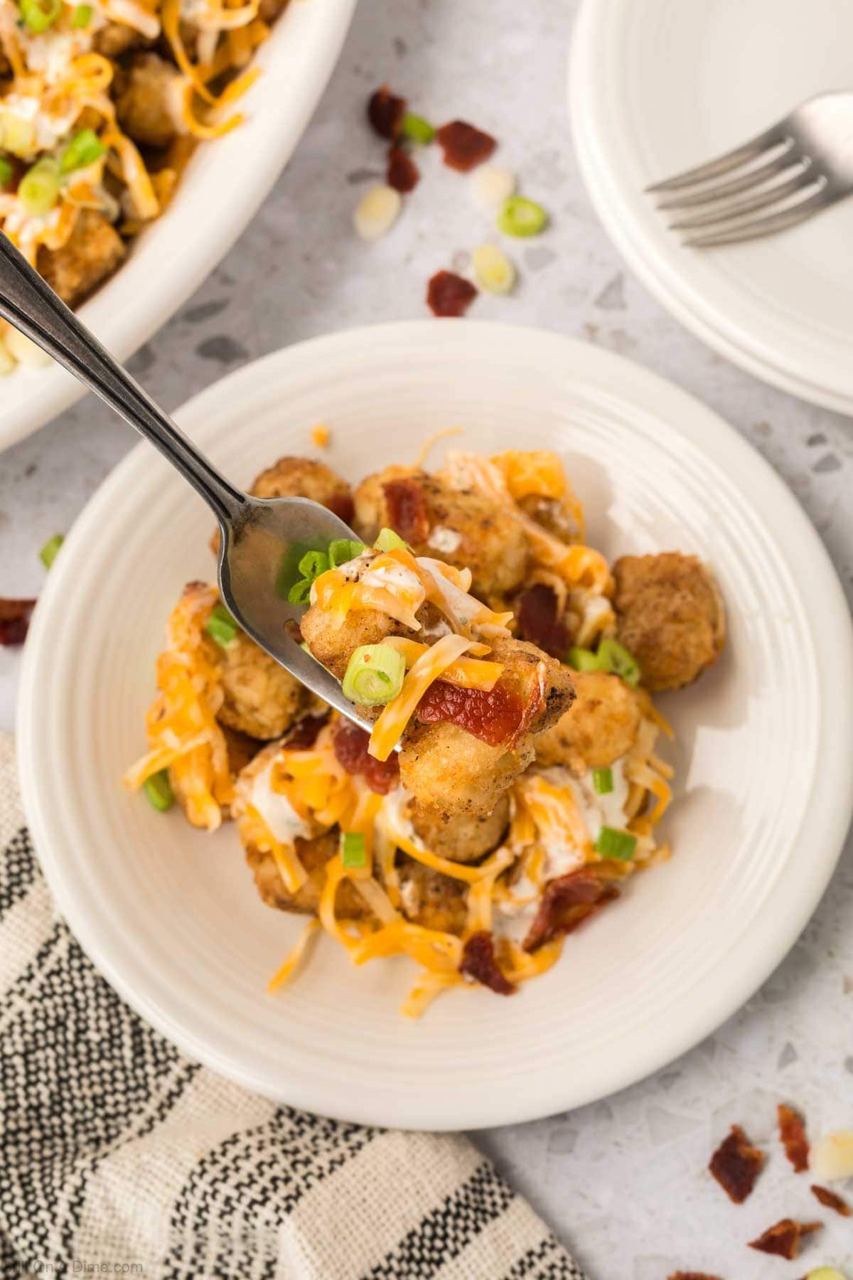 Serving of Loaded Tater Tots on a plate with a bite on a fork