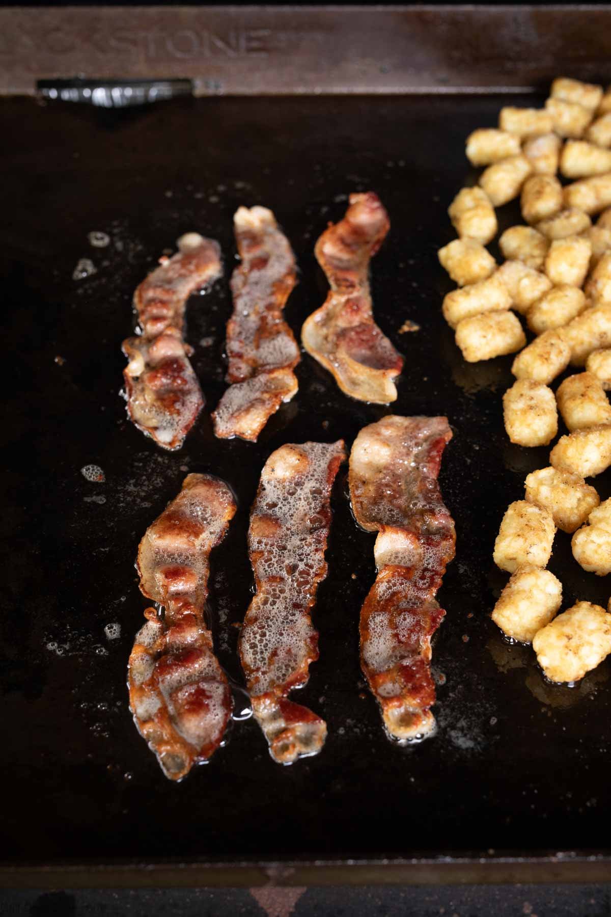 Cooking the strips of bacon on the griddle with tots on the side
