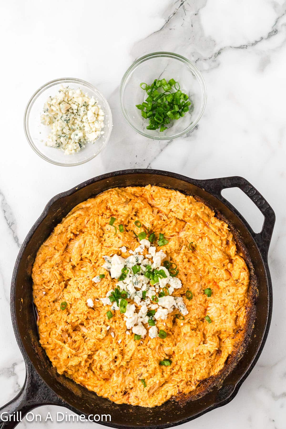 Smoked Buffalo Chicken Dip in a cast iron skillet topped with blue cheese crumbles and chopped green onions