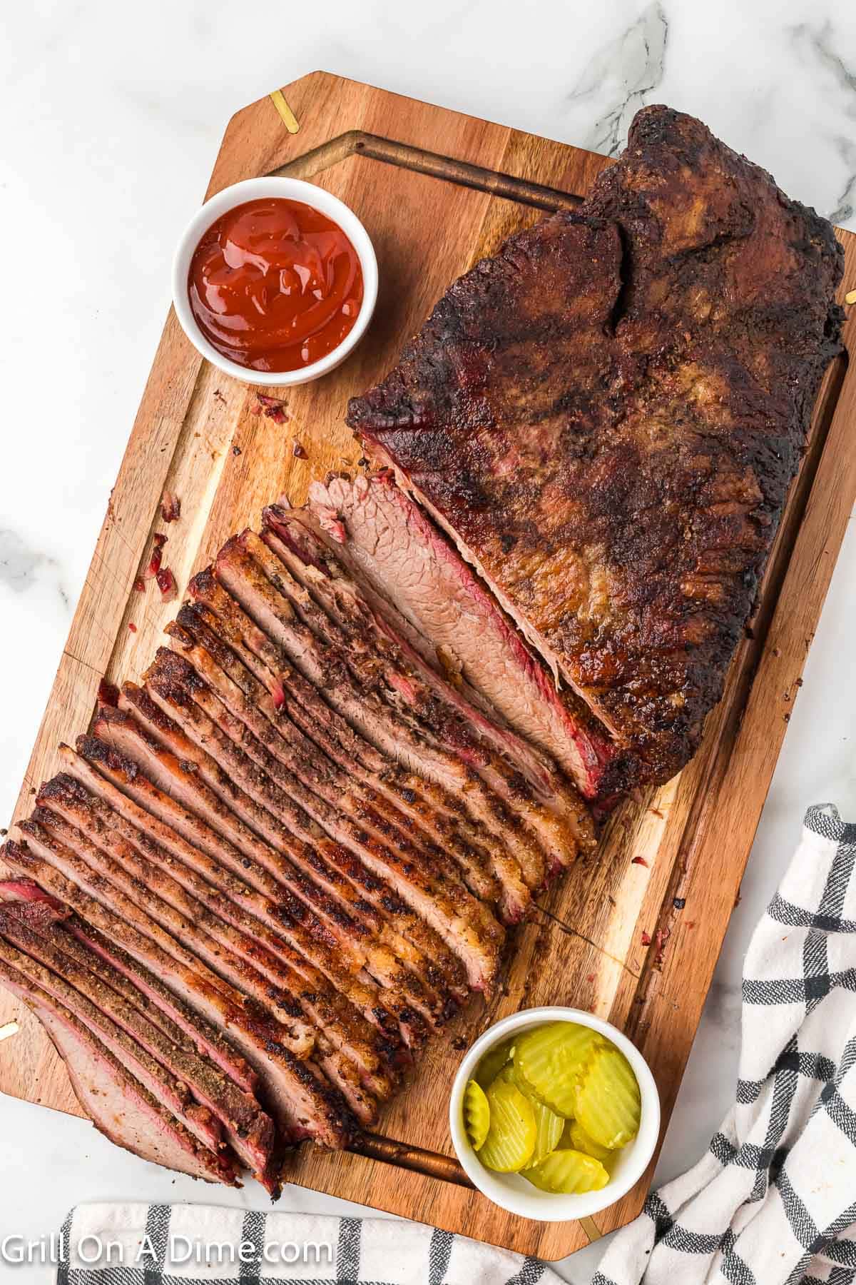 Sliced brisket on a cutting board with small bowls of slice pickles and ketchup