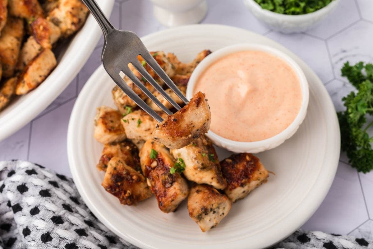 Golden Brown Chicken bites on a plate with a bite on a fork and a side of dipping sauce