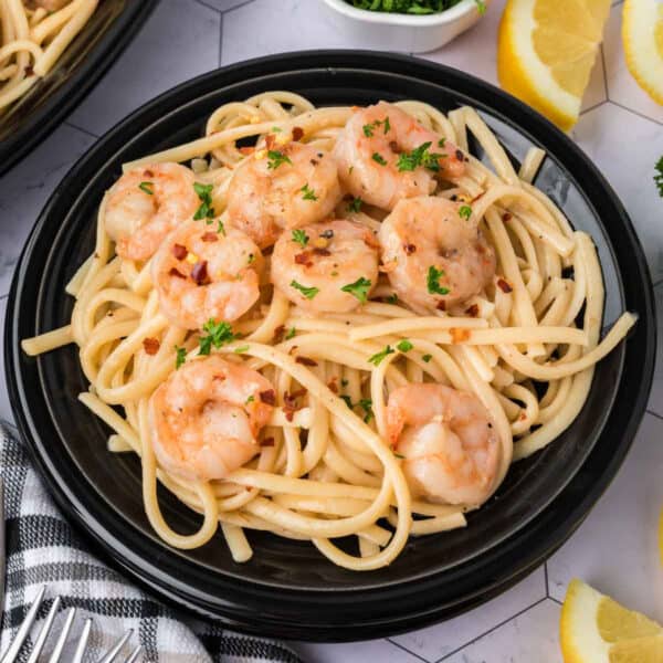 A plate of pasta with shrimp and lemon wedges.