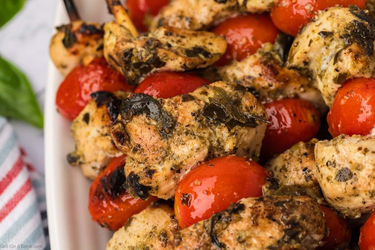Grilled chunks of chicken with cherry tomatoes on wooden skewers stacked on a plate
