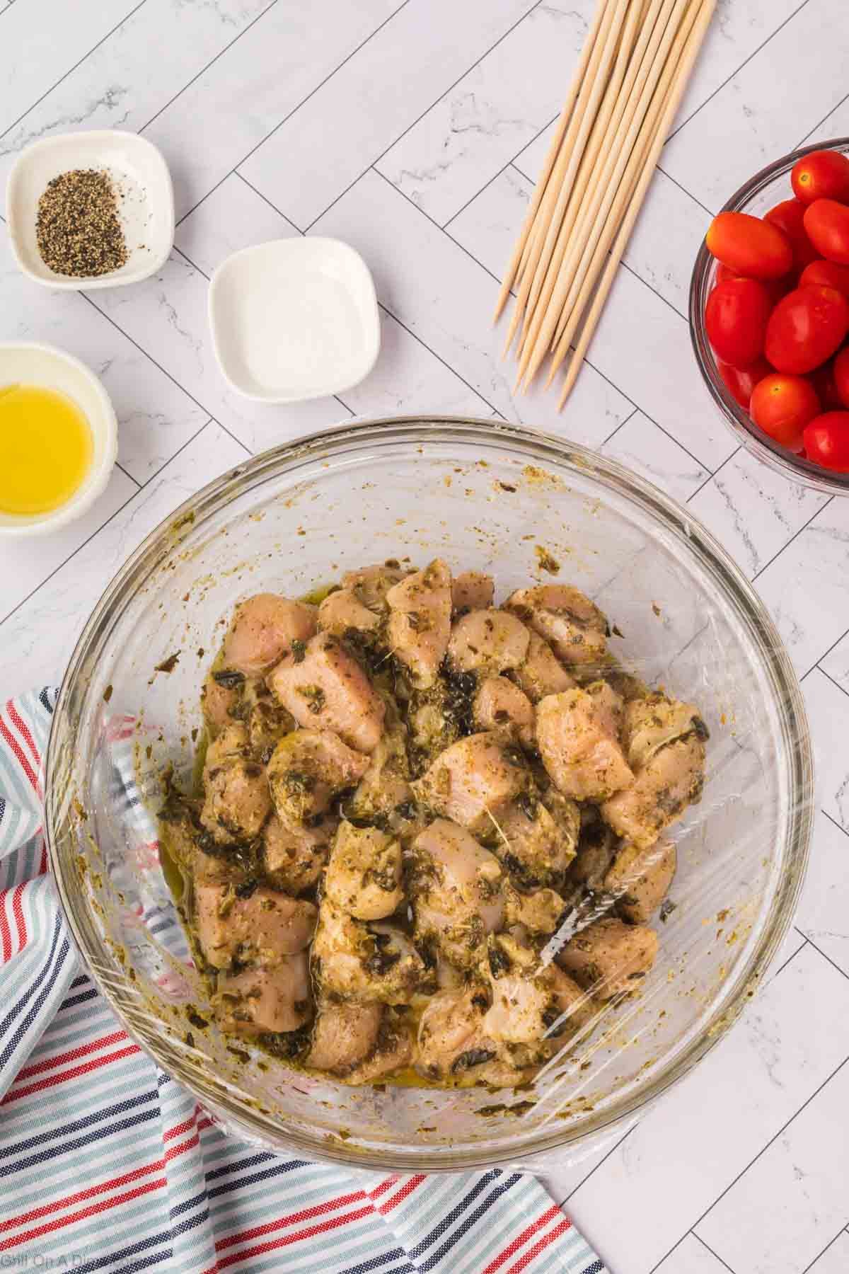Raw chicken chunks in the bowl with the pesto sauce covered with plastic wrap