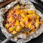 A plate of foil wrapped potatoes and ham.