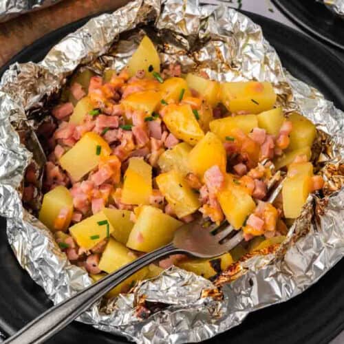 A plate of foil wrapped potatoes and ham.