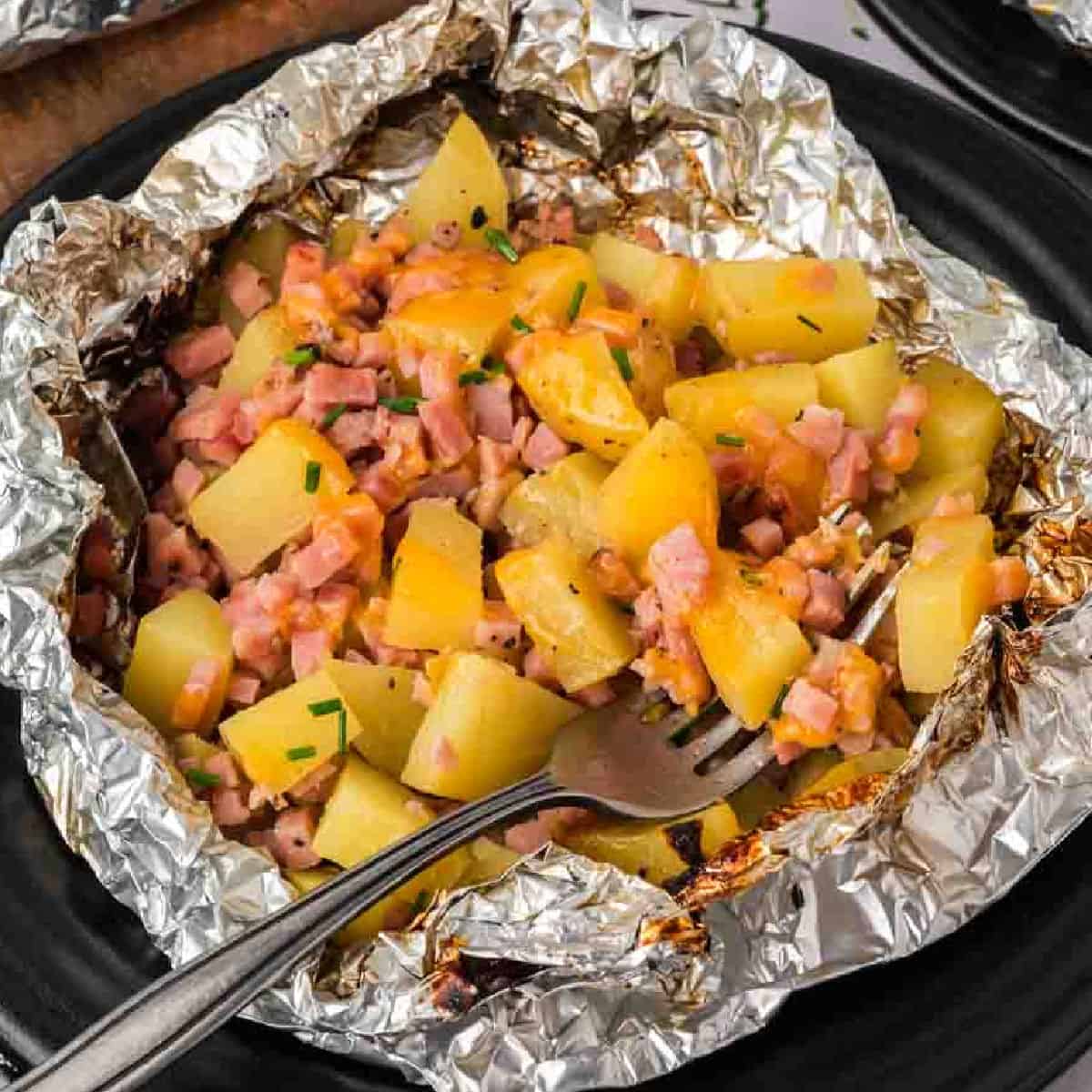 A plate of foil wrapped potatoes and ham.