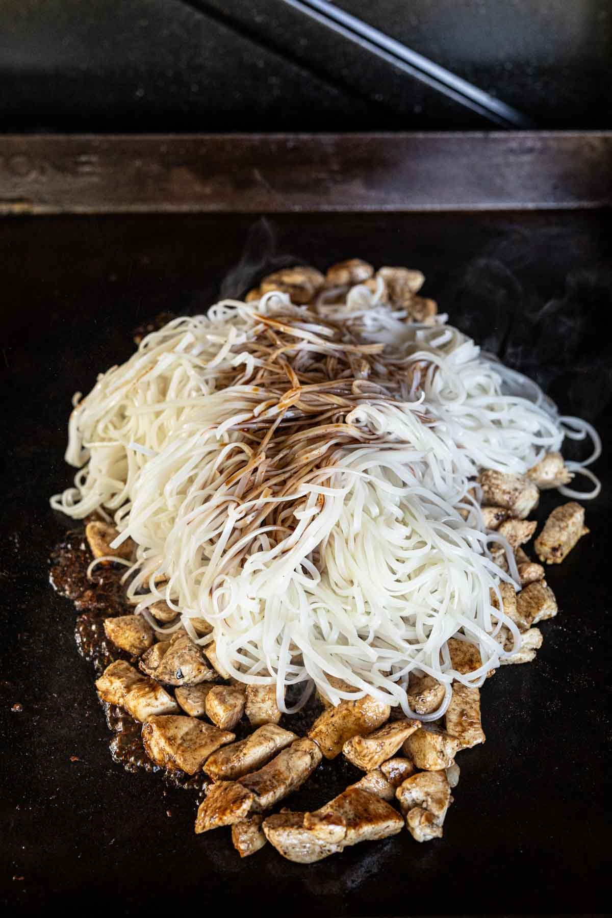 Cooking chicken on the griddle topped with cooked noodles