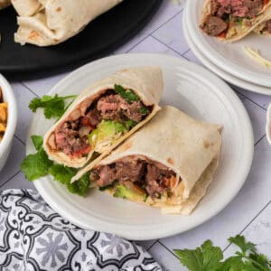 Two beef burritos on white plates with chips and salsa.