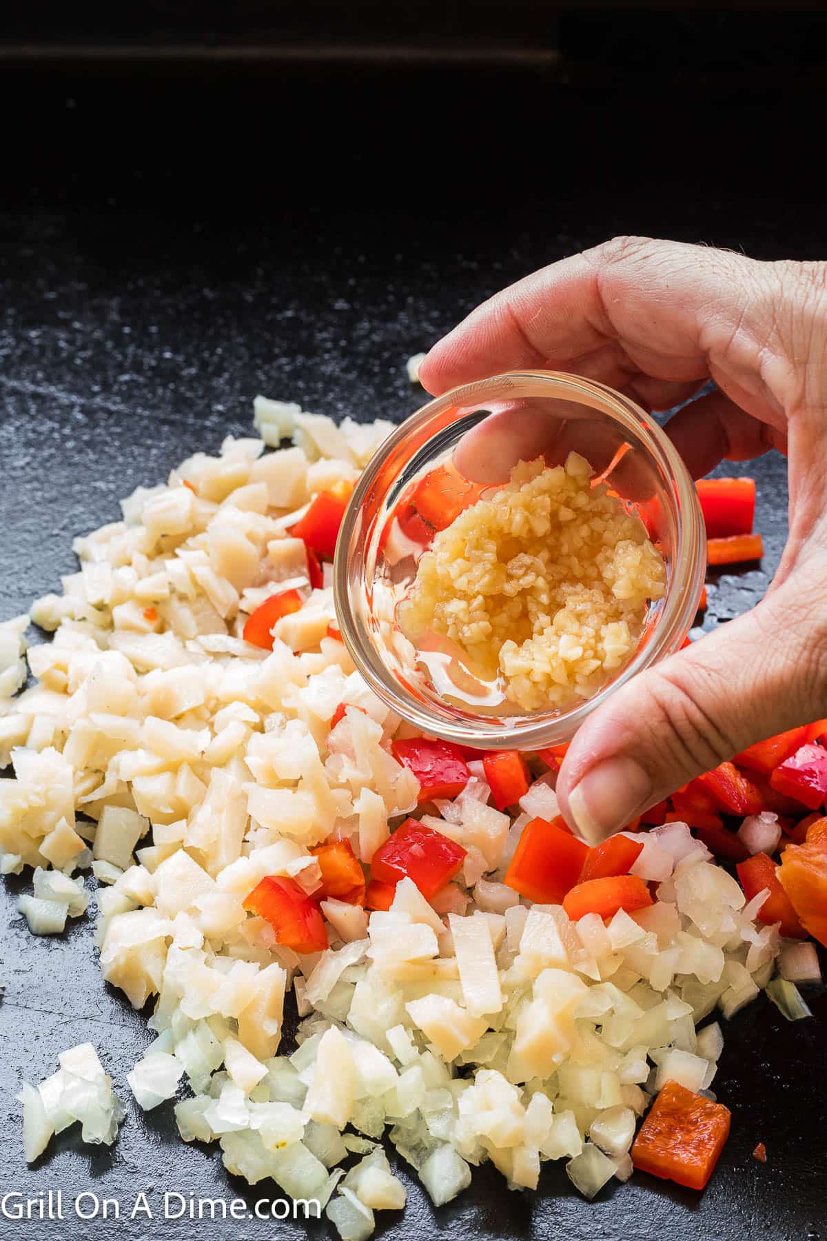 Pouring minced garlic onto the cook veggies on the Blackstone