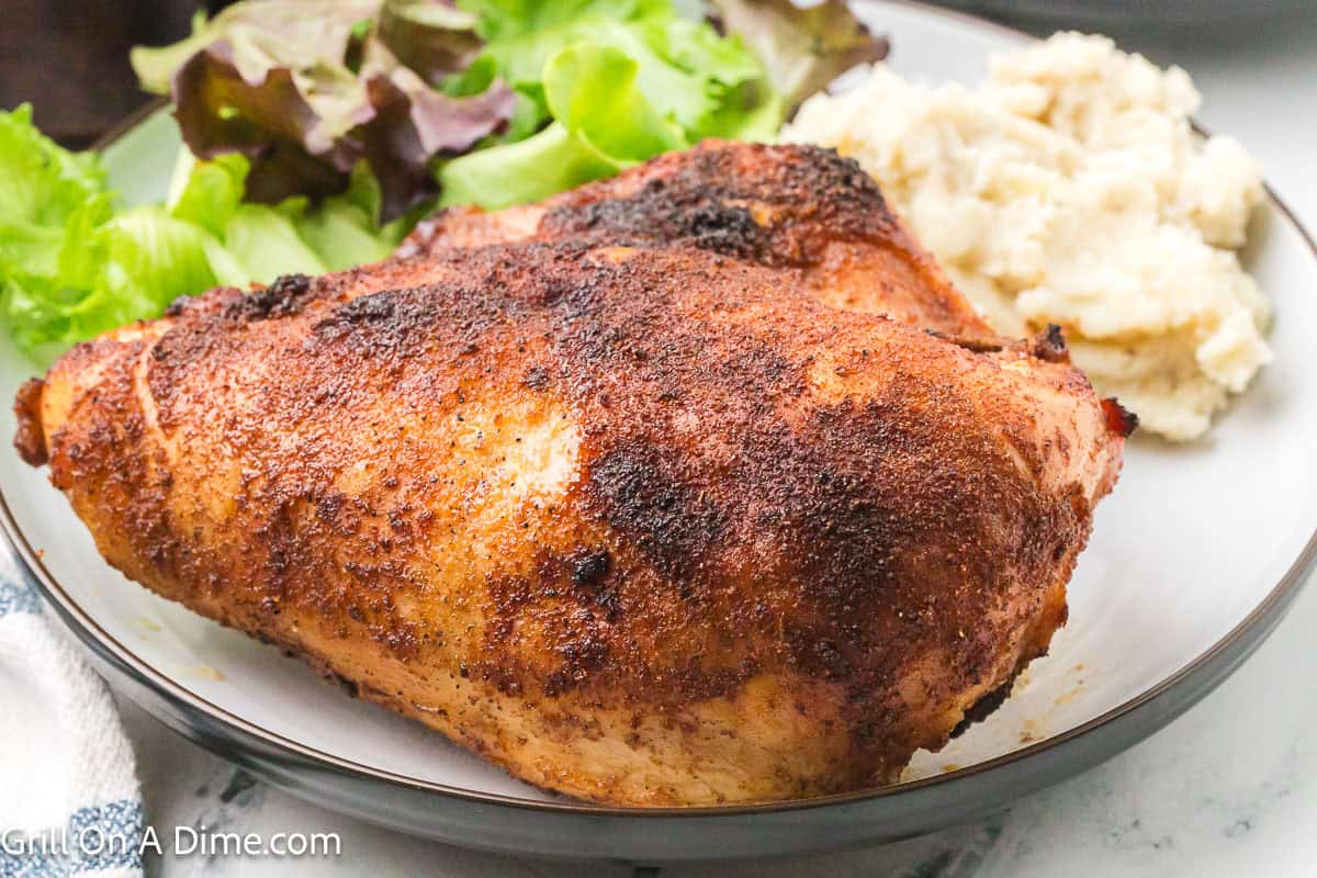 Smoked bone-in chicken breast on a plate with mashed potatoes and green salad