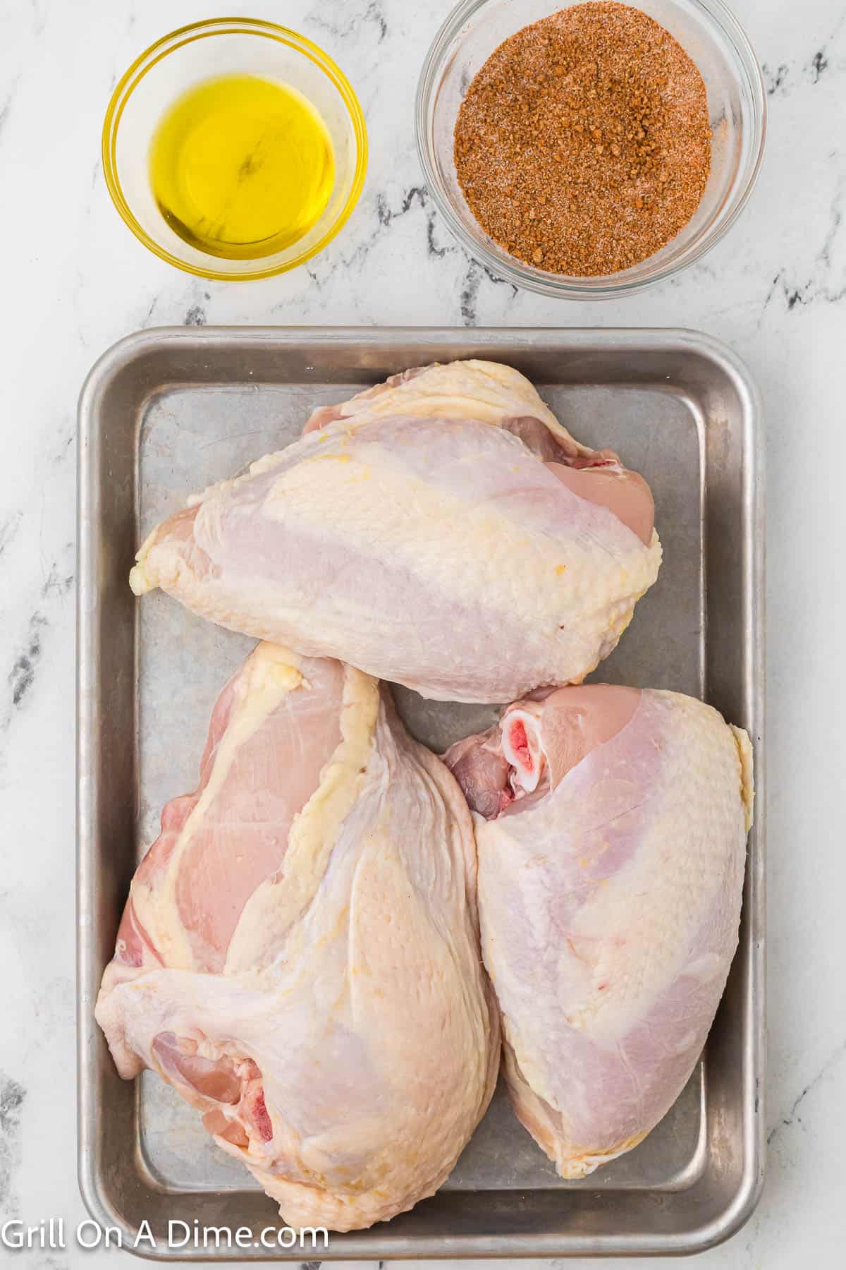 Bone In Chicken breast on a baking sheet with a bowl of oil and spices on the side