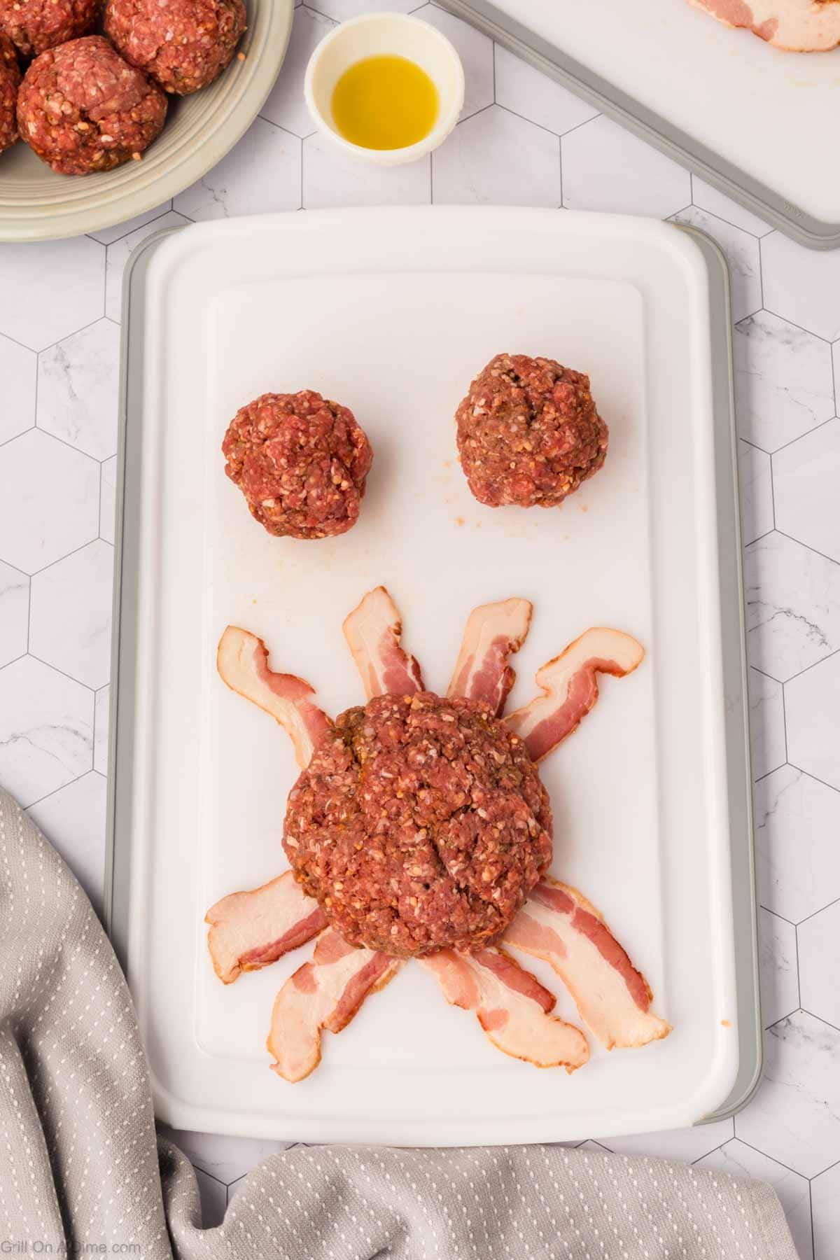 Ground beef pattie on strips of bacon with two ground beef balls on the side