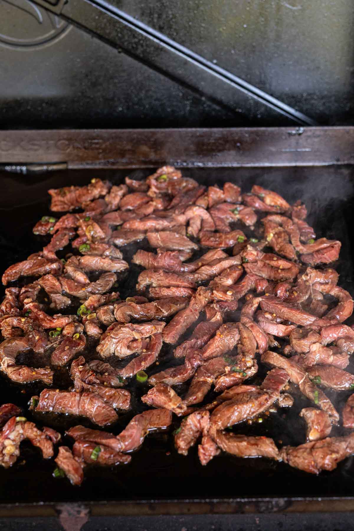 Placing the strips of steak on to the flat top grill
