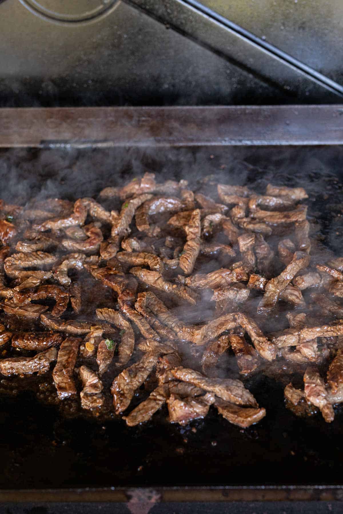 Cooked strips of steak on the flat top grill