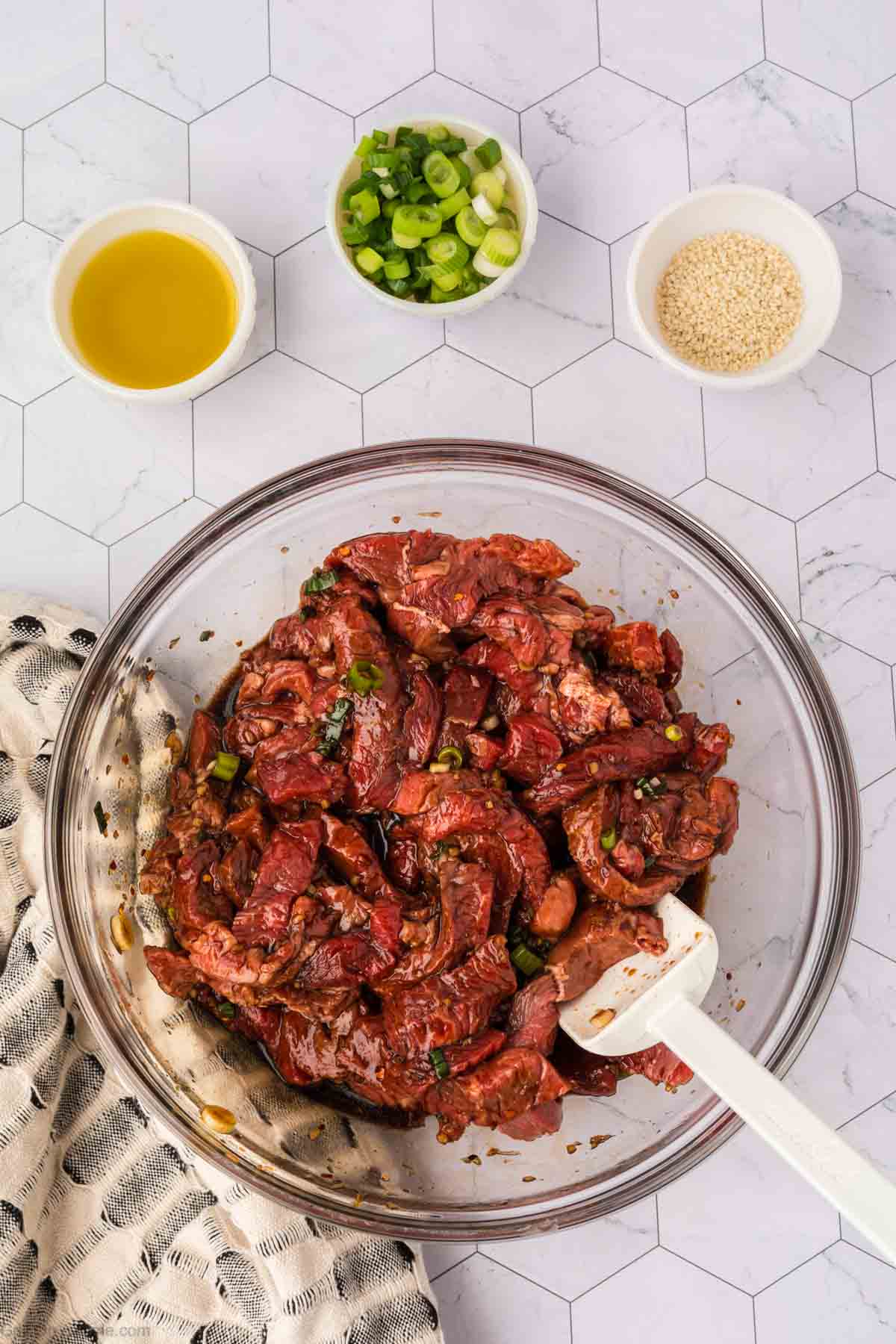 Placing the strips of steak in a bowl with the marinade with small bowls of oil, greens onions and sesame seeds on the side