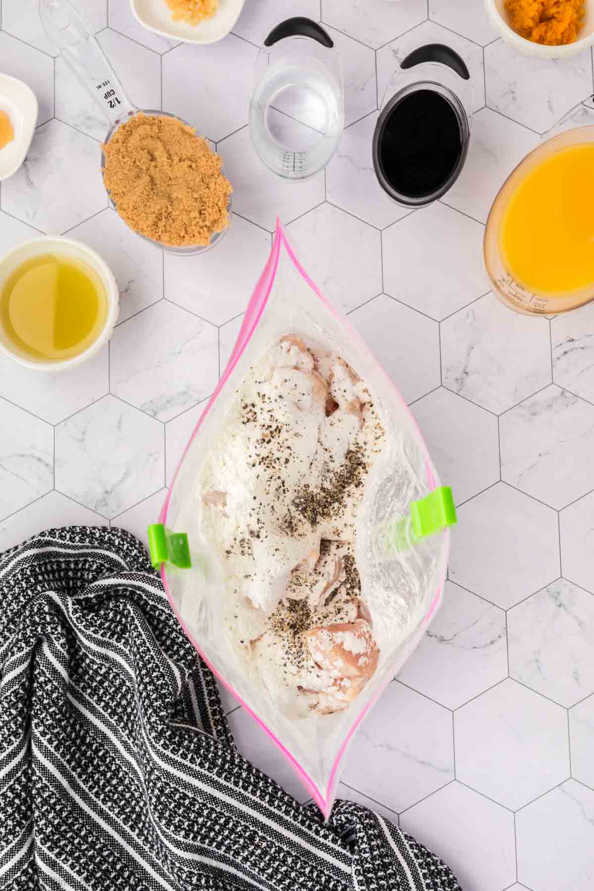 Chicken mixed with cornstarch, salt, and pepper in a zip lock bag with bowls of soy sauce, brown sugar, oil and orange juice on teh side