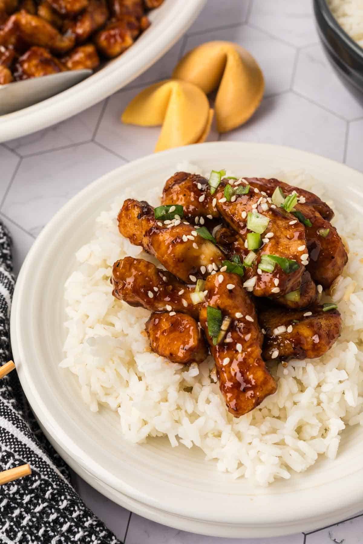 Orange Chicken over rice on a plate topped with green onions and sesame seeds