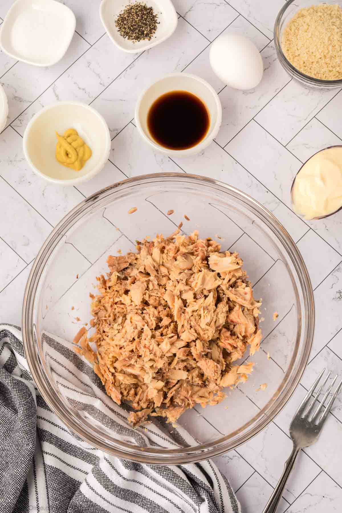 Shredded salmon in a bowl with small bowls of oil and seasoning on the side