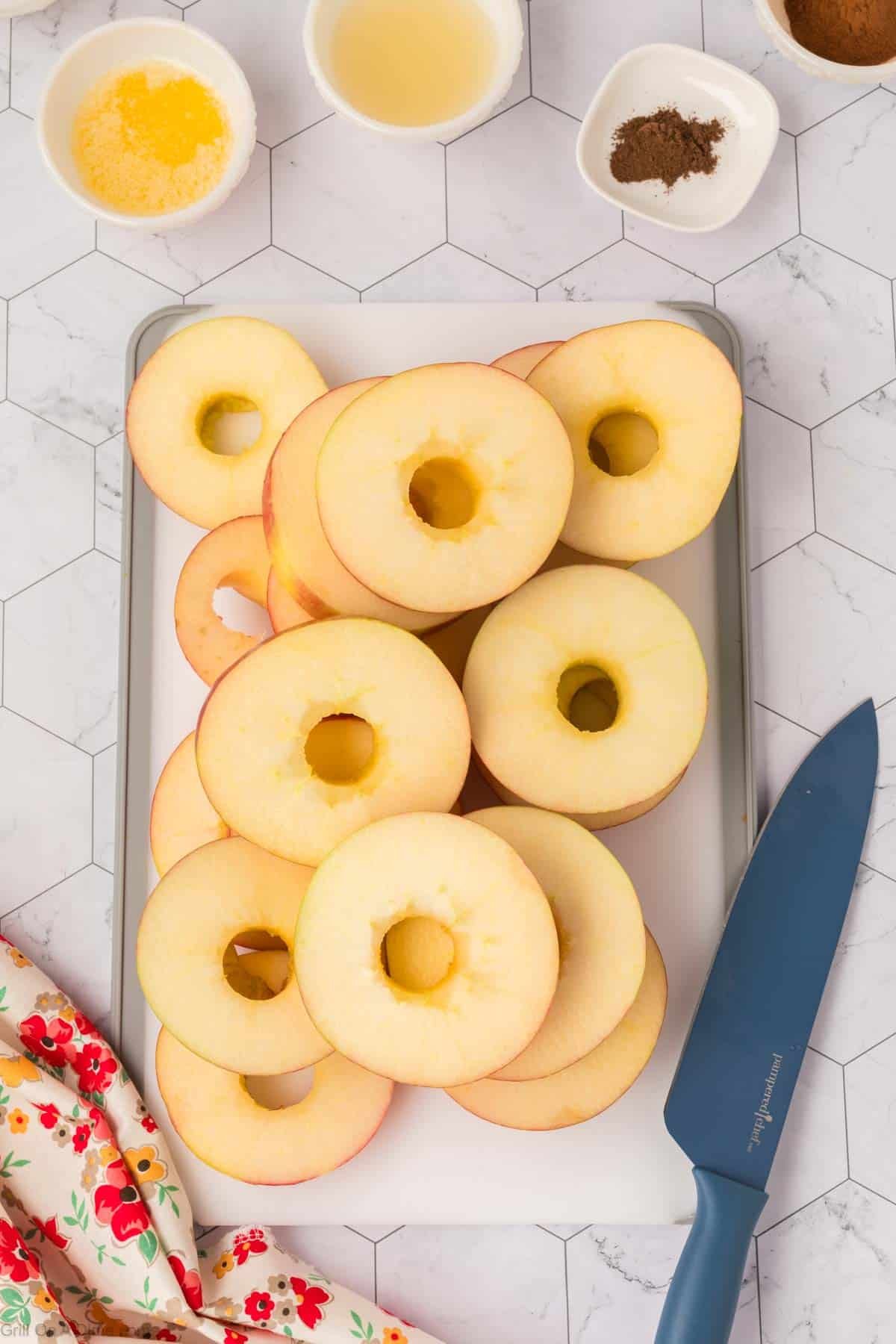 Apple slices on a cutting board with small bowls of spices and oil on the side