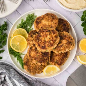 Salmon Patties stacked on a plate with slices of lemon on the side