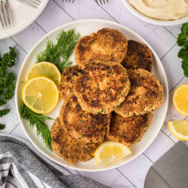 Salmon Patties stacked on a plate with slices of lemon on the side