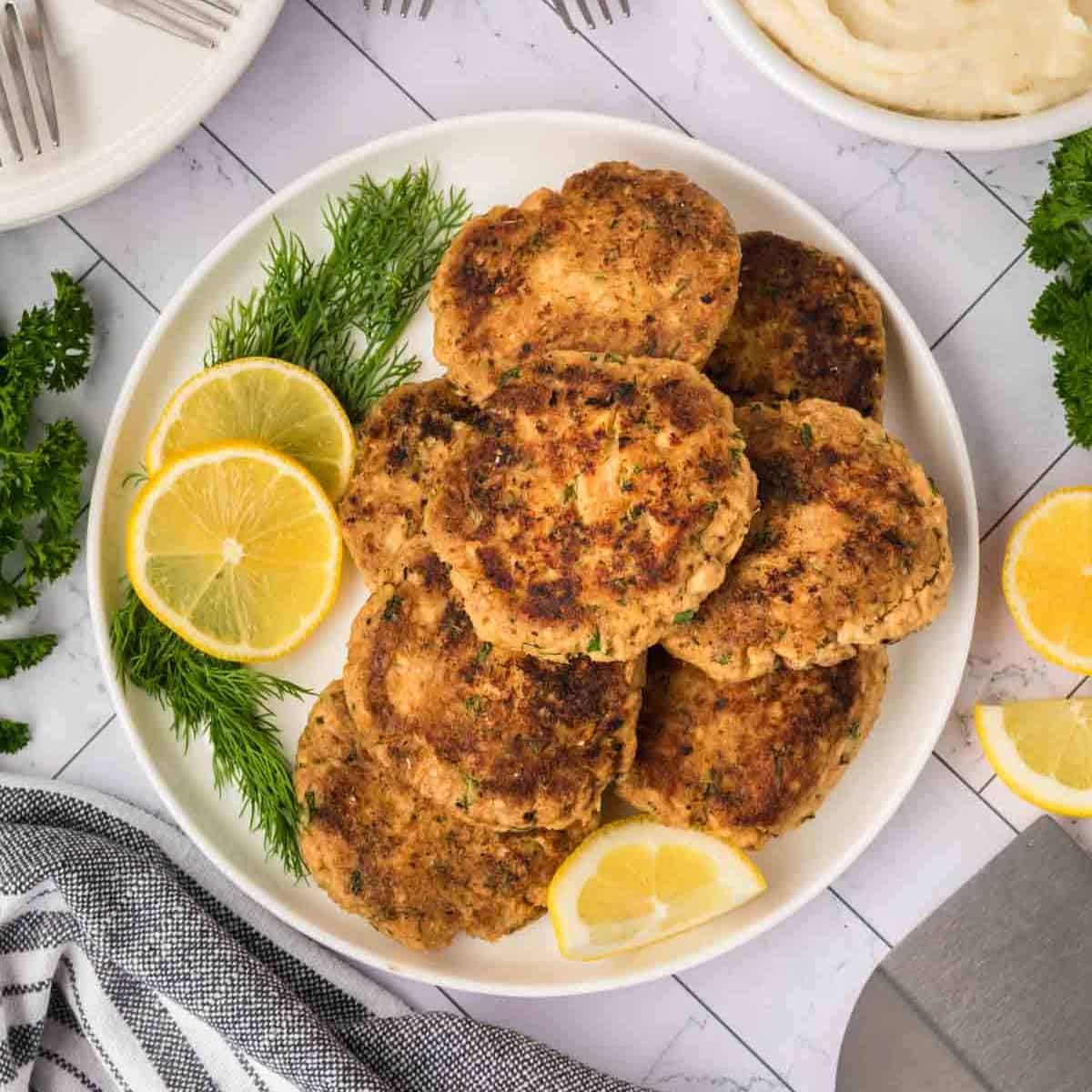Salmon Patties stacked on a plate with slices of lemon on the side