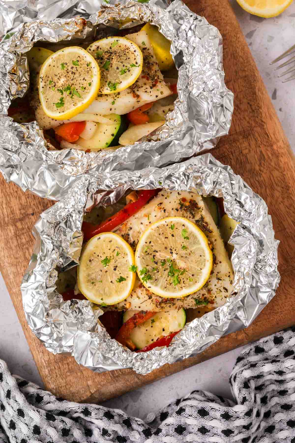 Fish and veggie foil packets on a wooden board