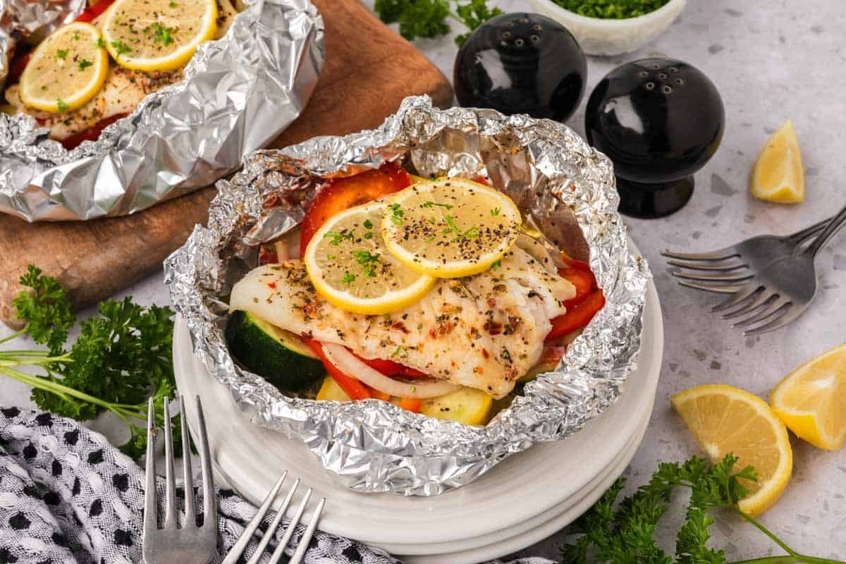 Cooked fish and veggies topped with lemon slices and seasoning on a piece of foil