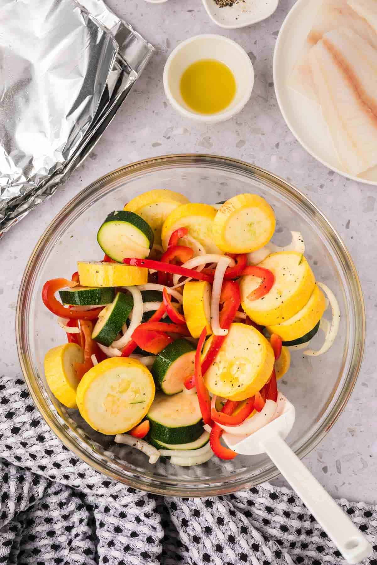 Slice squash, zucchini, red bell pepper, onions in a bowl with spices