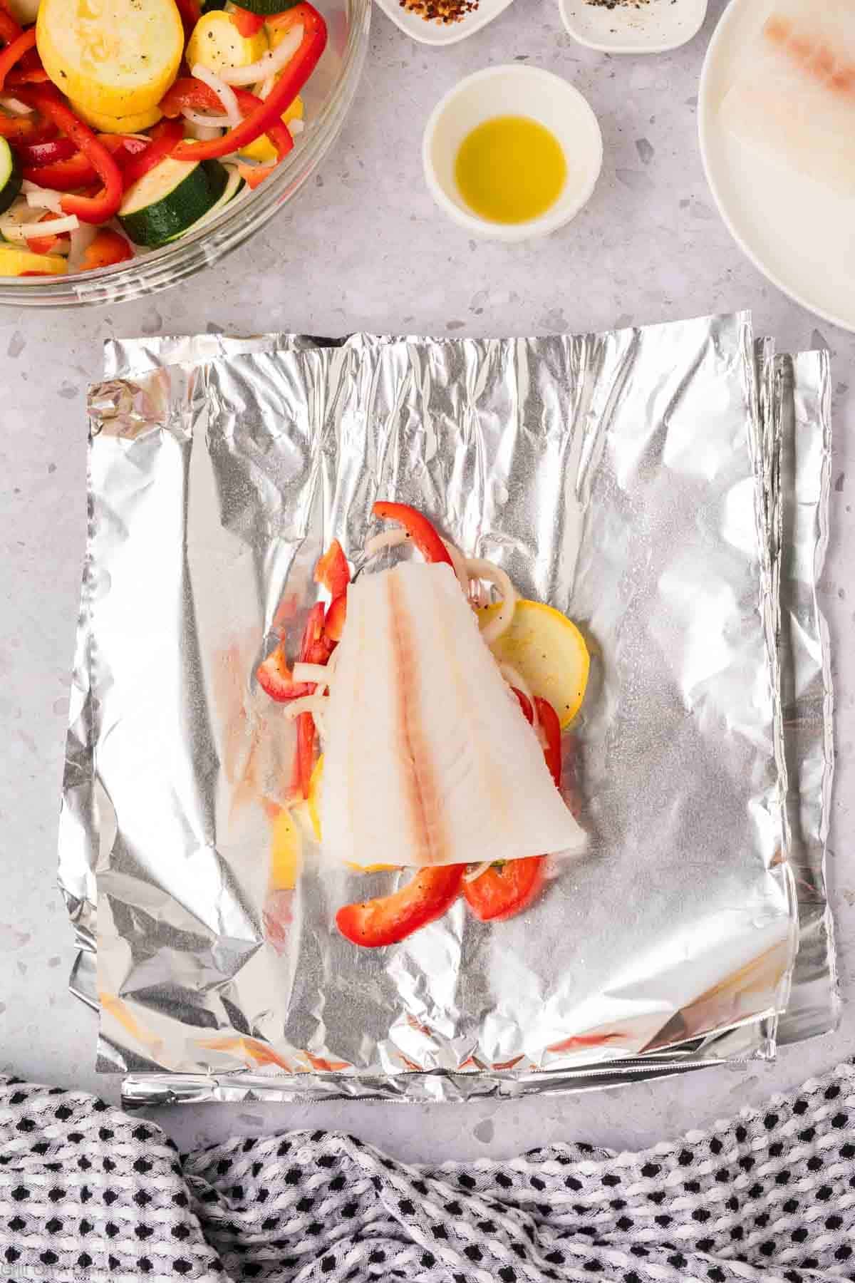 White fish placed on top of the fresh veggies on a piece of foil