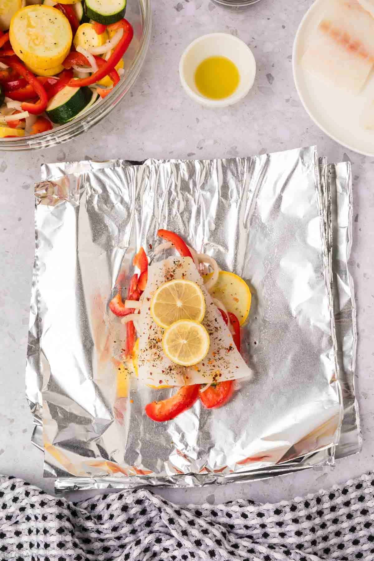 Slice lemon placed on top of white fish and veggies on a piece of foil