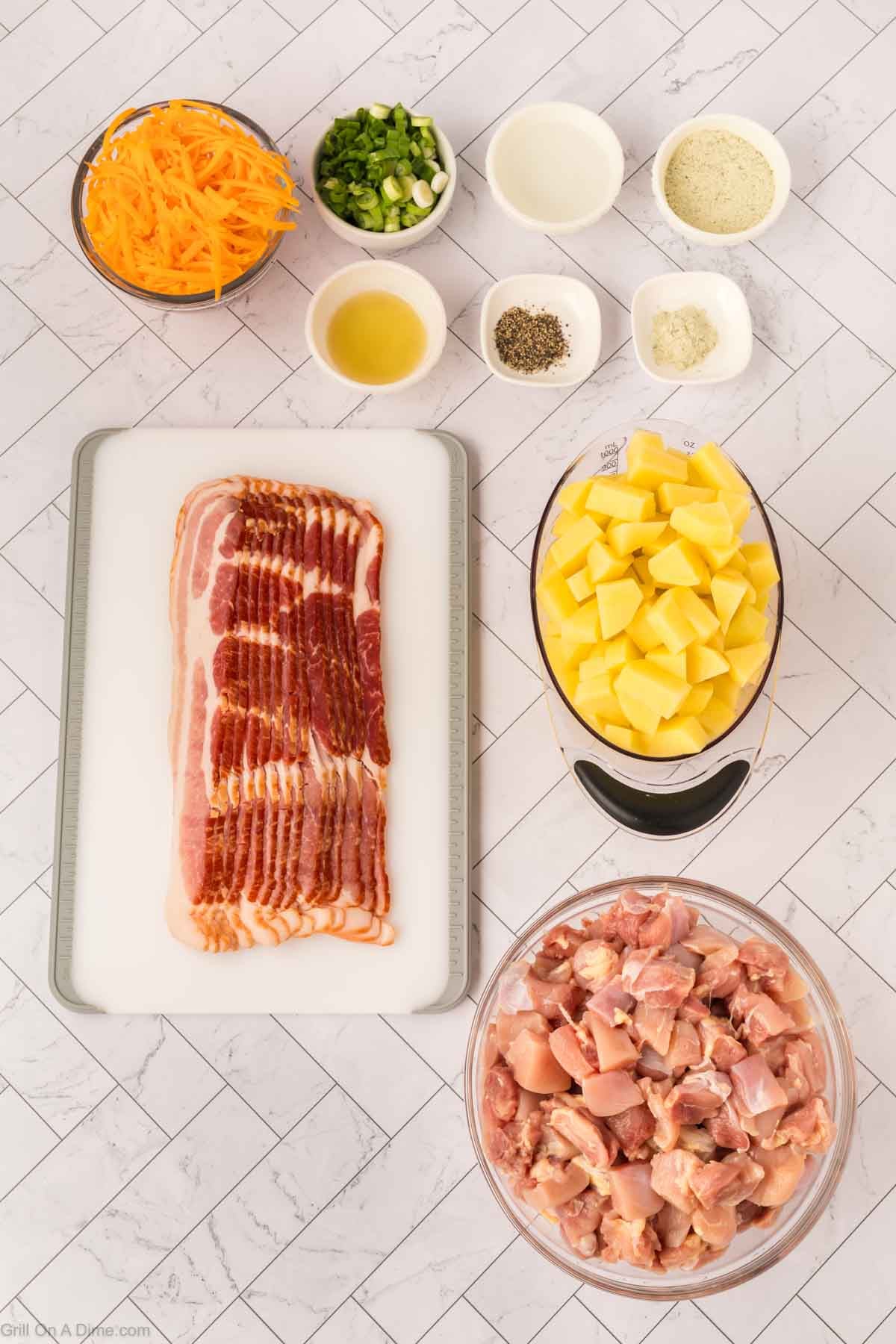 Top-down view of ingredients on a white surface: sliced bacon on a cutting board, diced potatoes, raw Blackstone Chicken pieces in a bowl, shredded cheese, chopped green onions, and small bowls of seasonings.
