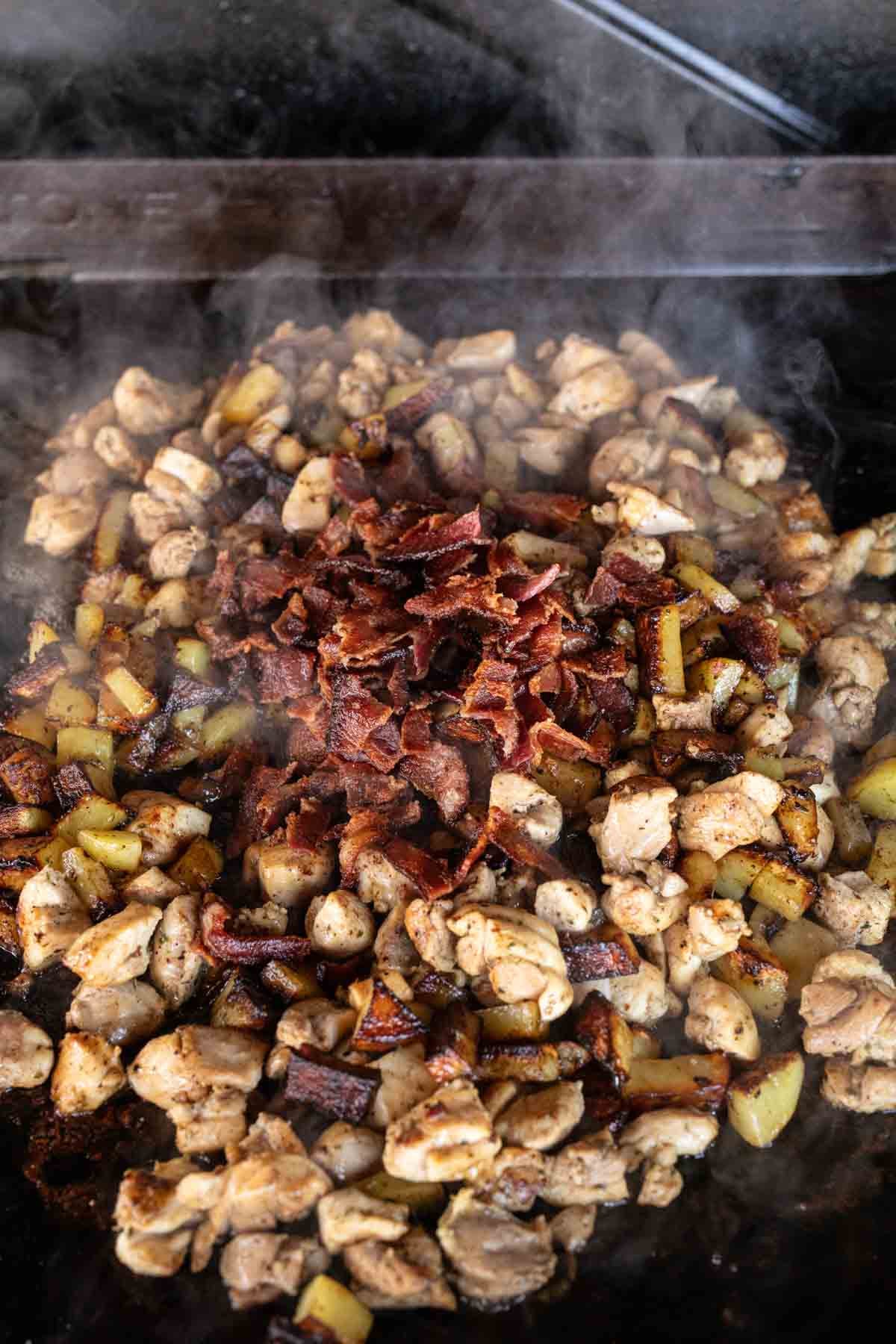 Diced chicken, crispy bacon, and small potato pieces sizzle together on a hot Blackstone griddle, capturing that signature smoky flavor of Blackstone chicken.