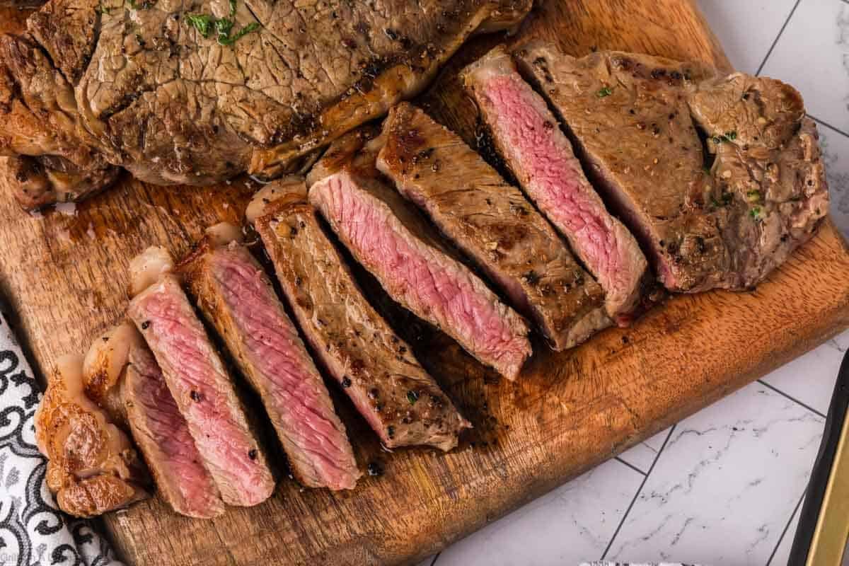 Sliced steak served on a wooden board, this Garlic Butter Steak is a mouthwatering Blackstone Recipe perfect for any occasion.