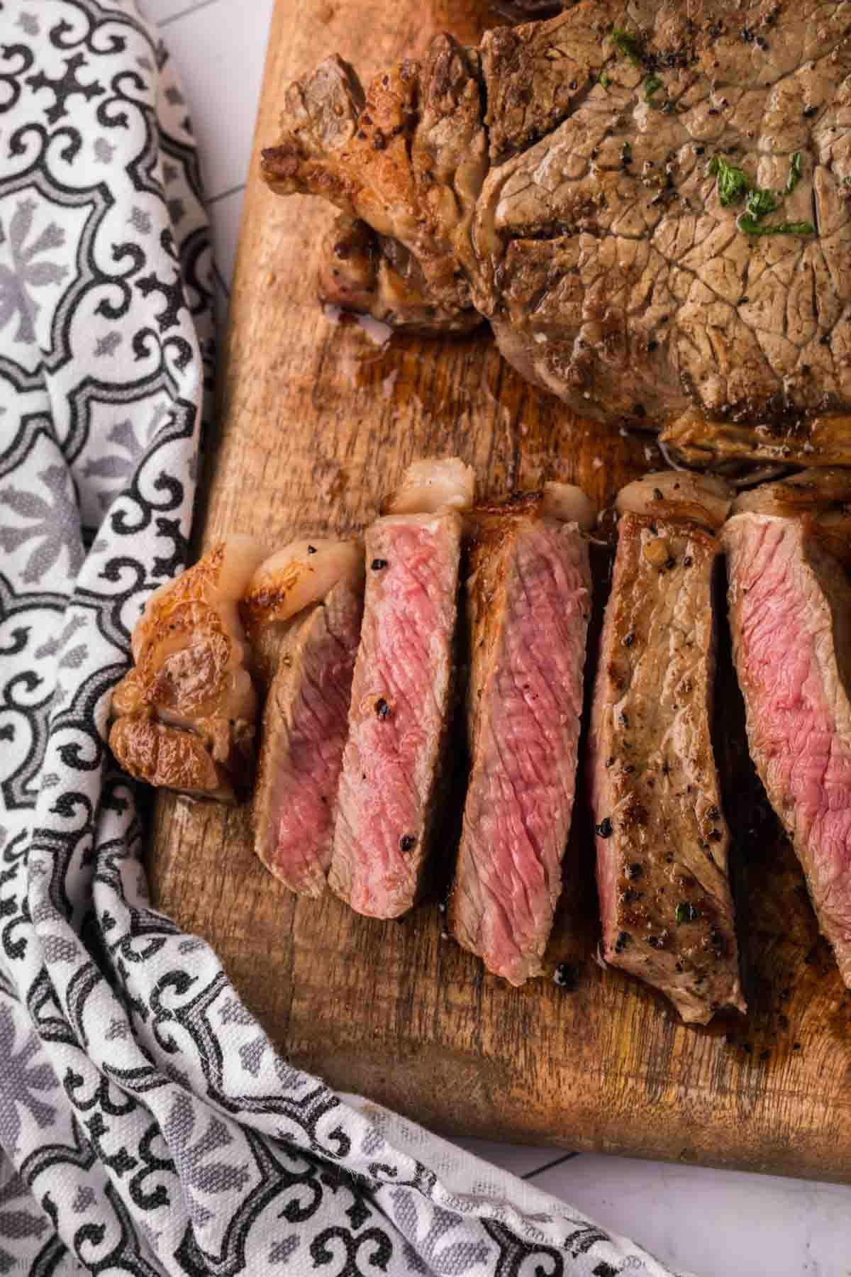 Sliced medium-rare Garlic Butter Steak on a wooden cutting board next to a black and white patterned cloth. The steak is juicy with a pink center, seared brown edges, and rich Blackstone Garlic Butter flavor.