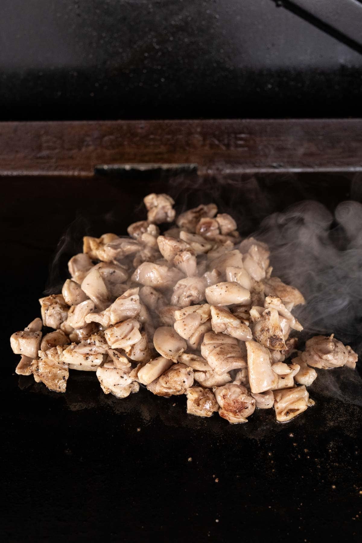 A pile of diced, cooked Blackstone Chicken sits steaming on a flat-top grill with a dark background.