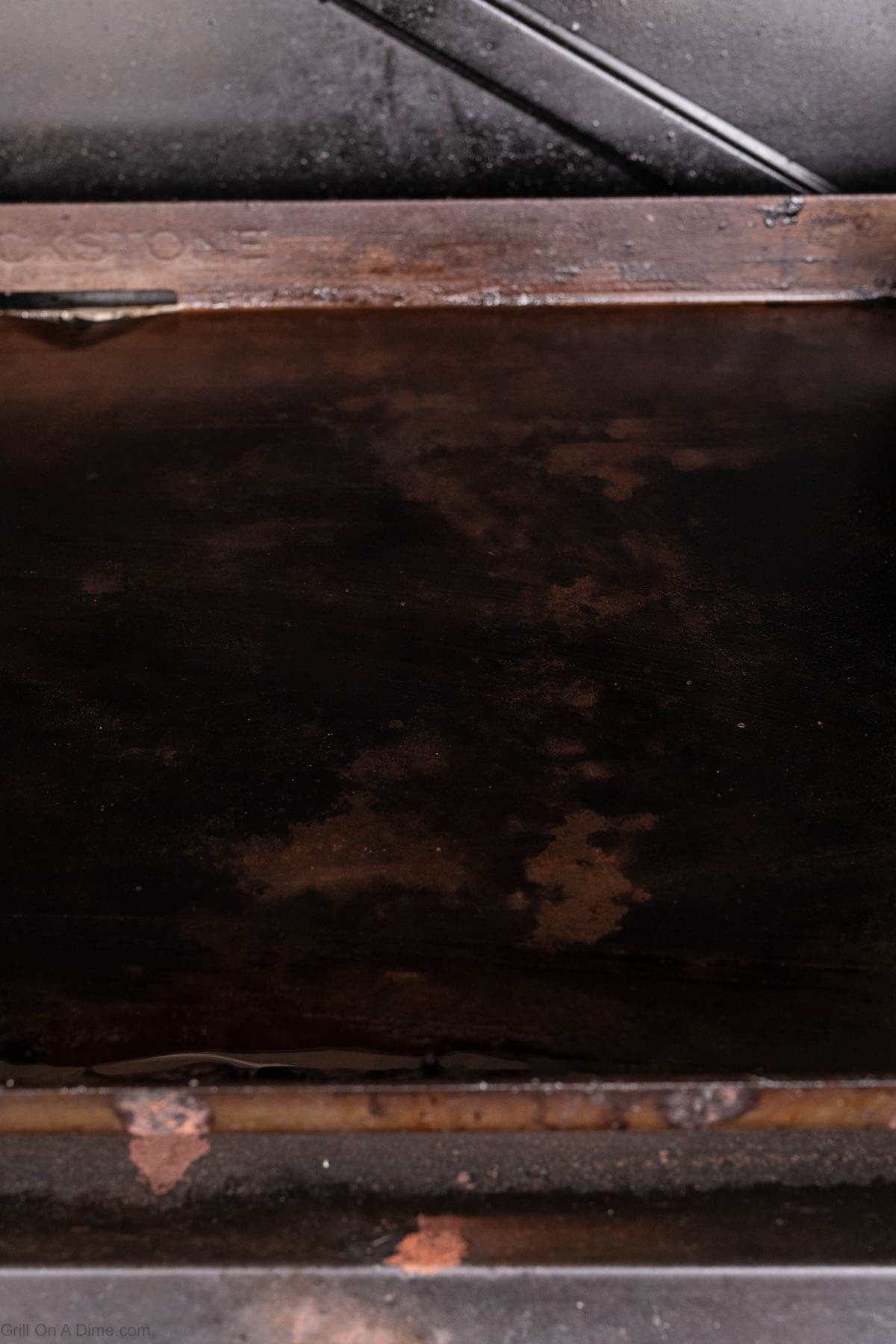 A close-up view of a flat, seasoned, and rust-stained Blackstone griddle surface, showing dark discoloration and patches of wear—the perfect backdrop for trying new Blackstone recipes like Honey Garlic Chicken.