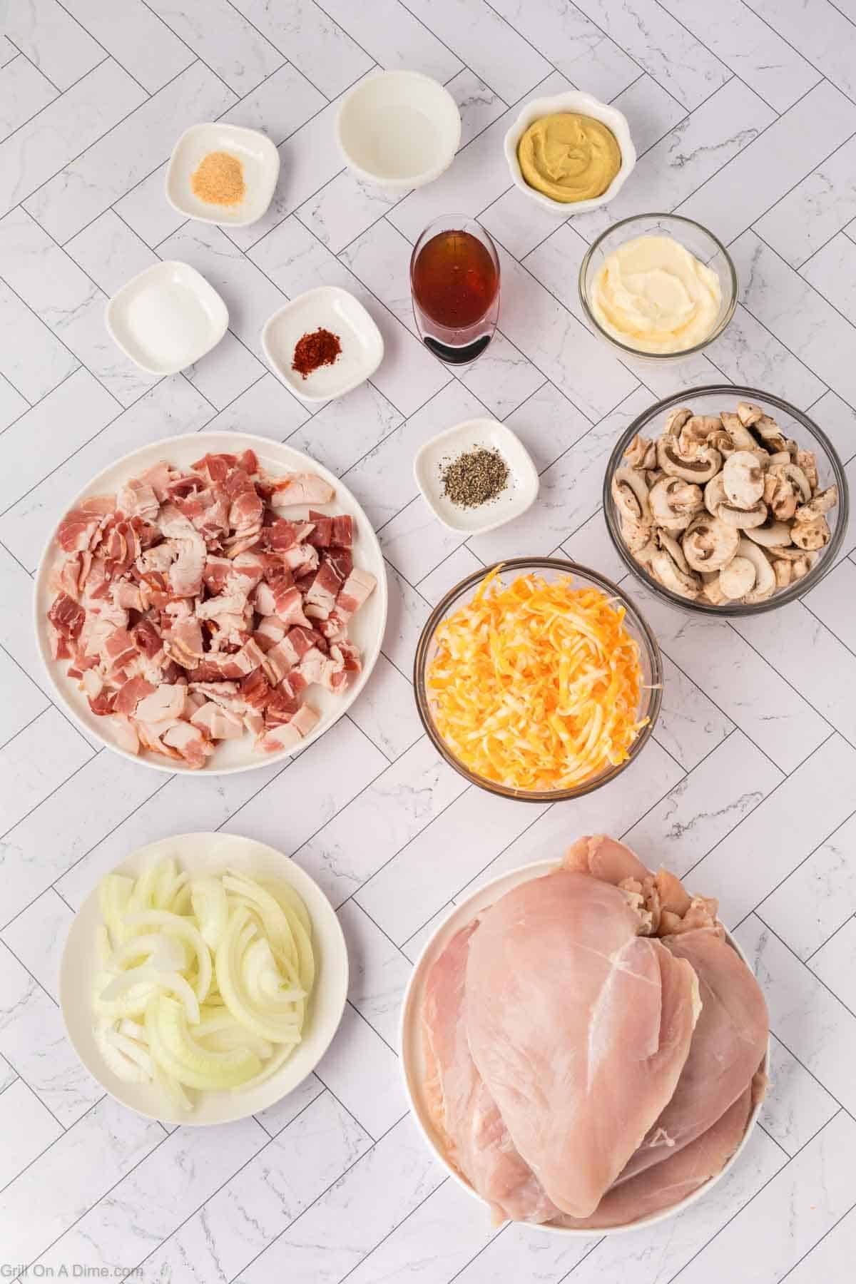 Ingredients on a white tile surface: raw chicken breasts, sliced onions, shredded cheese, mushrooms, chopped bacon, mayonnaise, mustard, oil, and small bowls of spices—everything you need for a flavorful Loaded Chicken recipe on your Blackstone griddle.