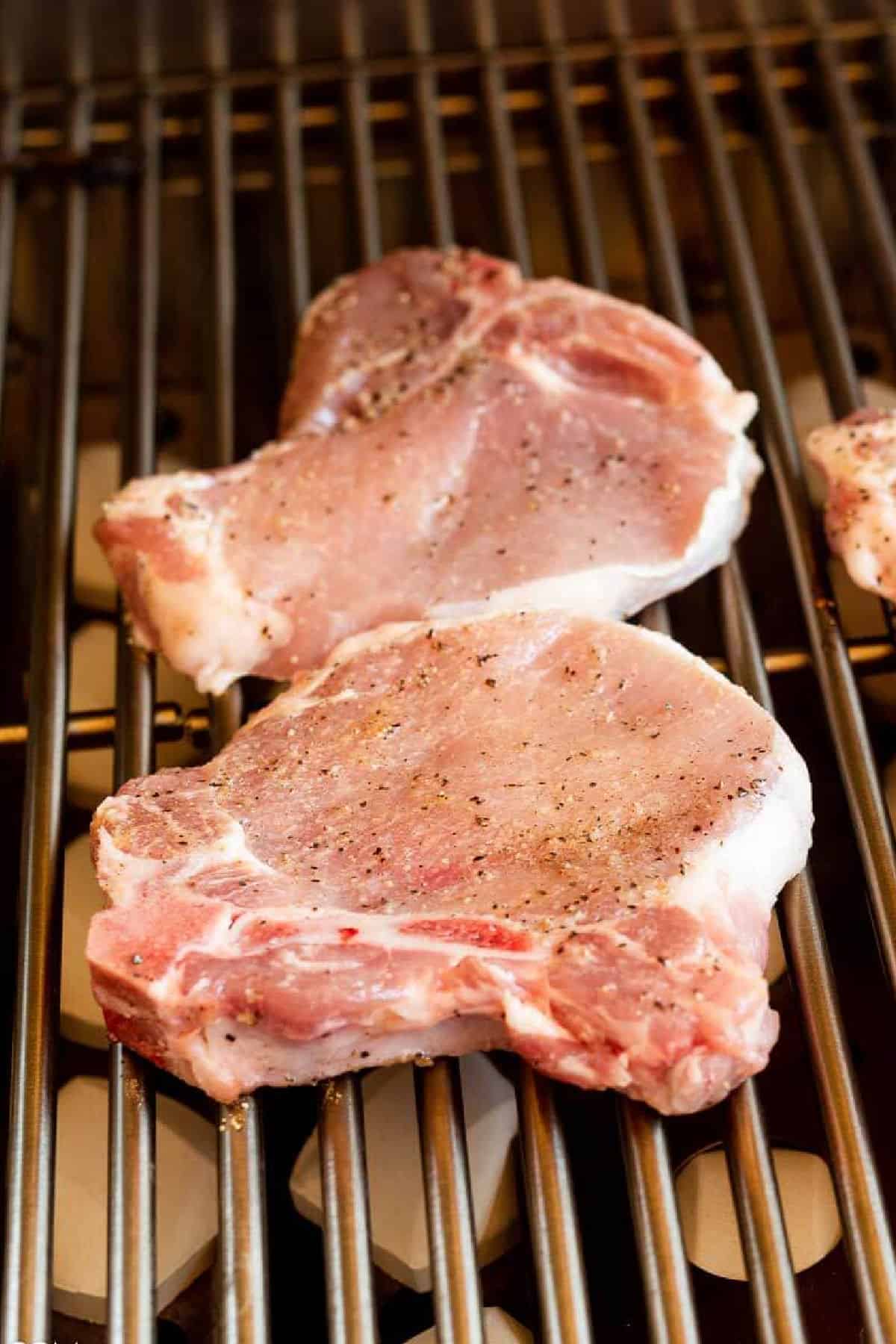 Two raw, seasoned Grilled BBQ Bone-In Pork Chops are placed on a metal grill grate, ready to be cooked.