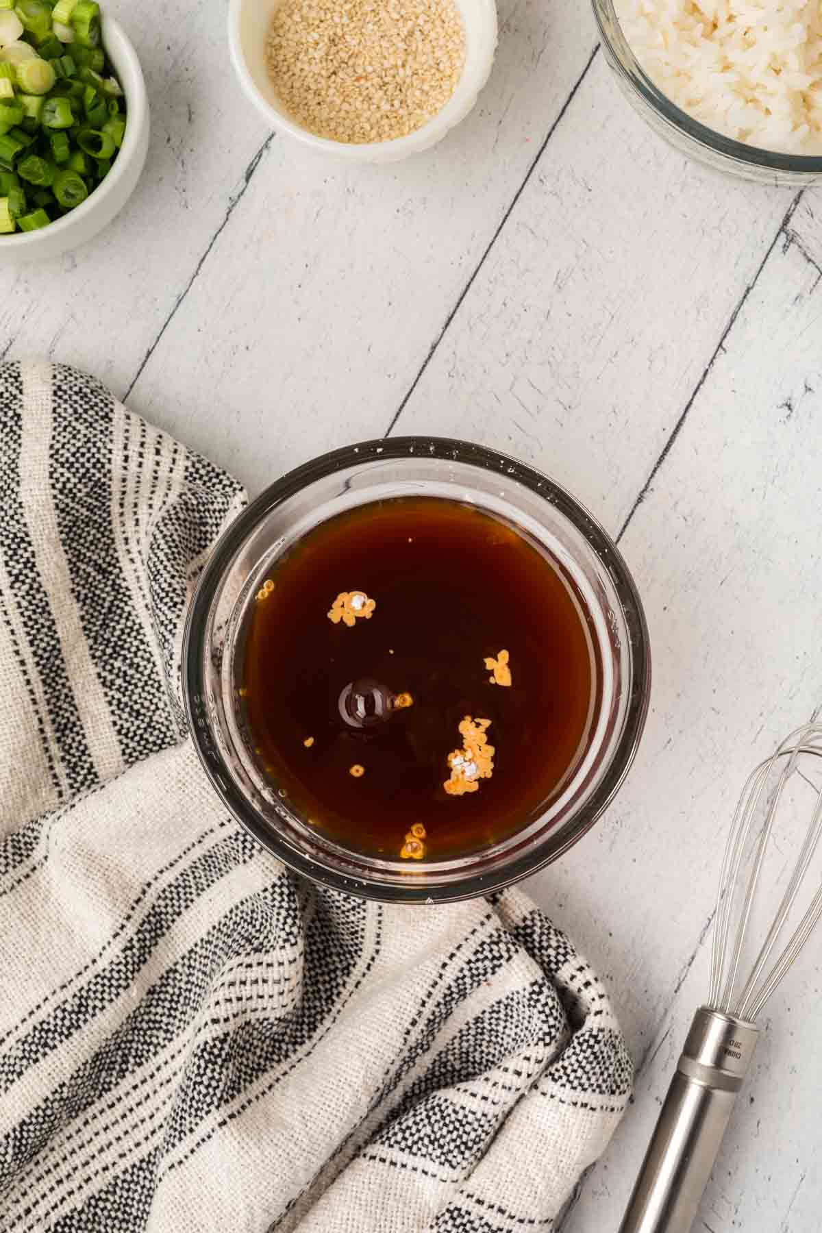 A small glass bowl filled with dark brown sauce and is topped with minced garlic.