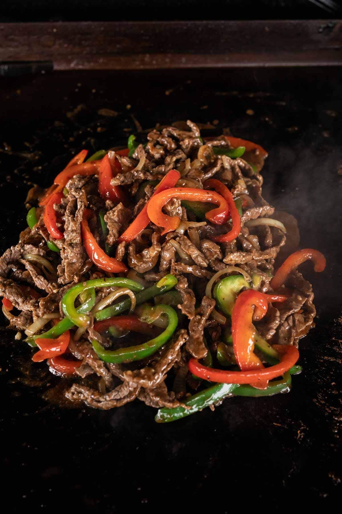 Sautéed strips of beef with red and green bell peppers cooking on a hot Blackstone griddle.