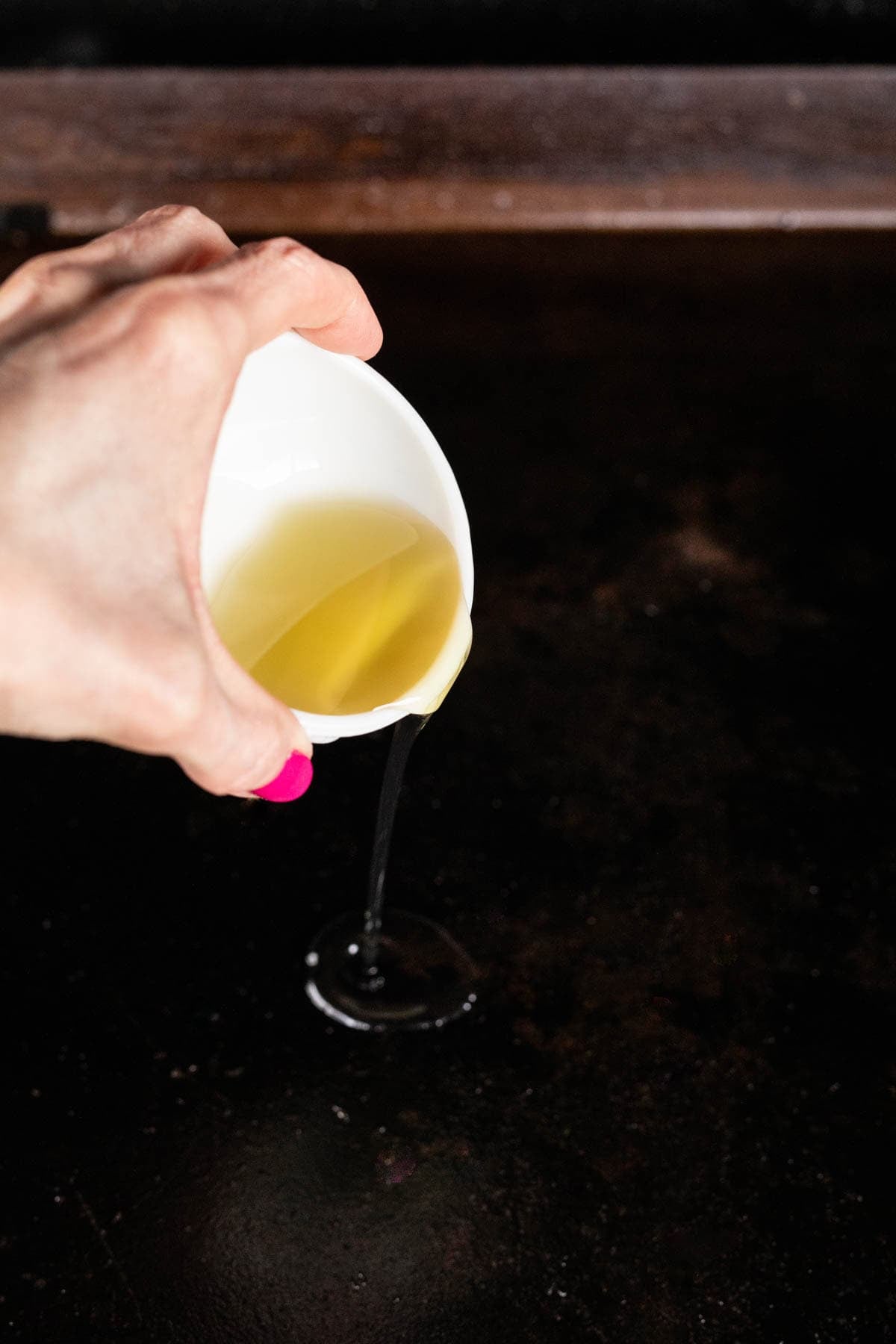 A hand pouring a small white bowl of oil onto the flat top griddle. 