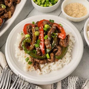 A white plate with white rice topped with Blackstone Pepper Steak.