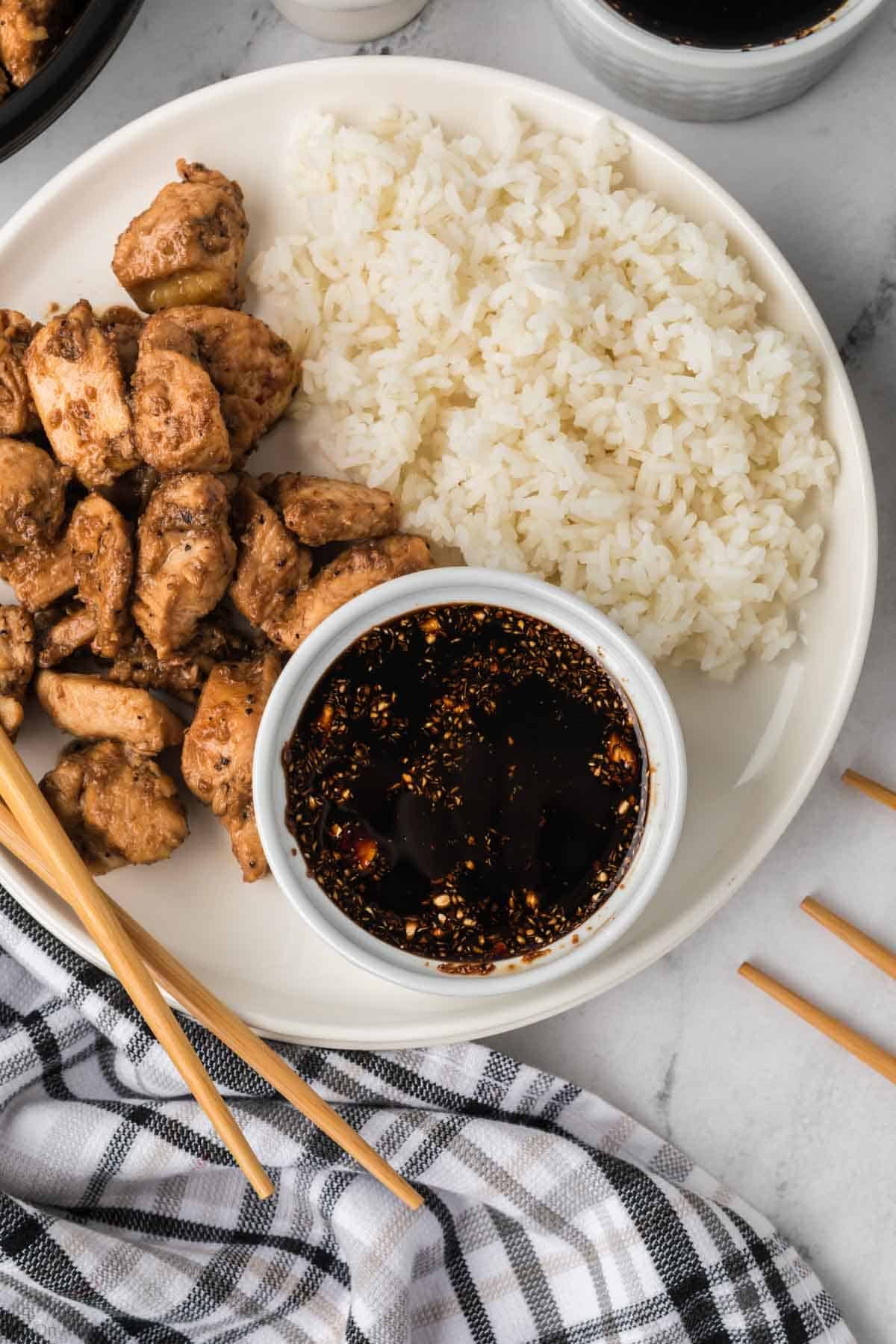 Hibachi chicken and white rice on a plate with a small bowl of dark sauce. 