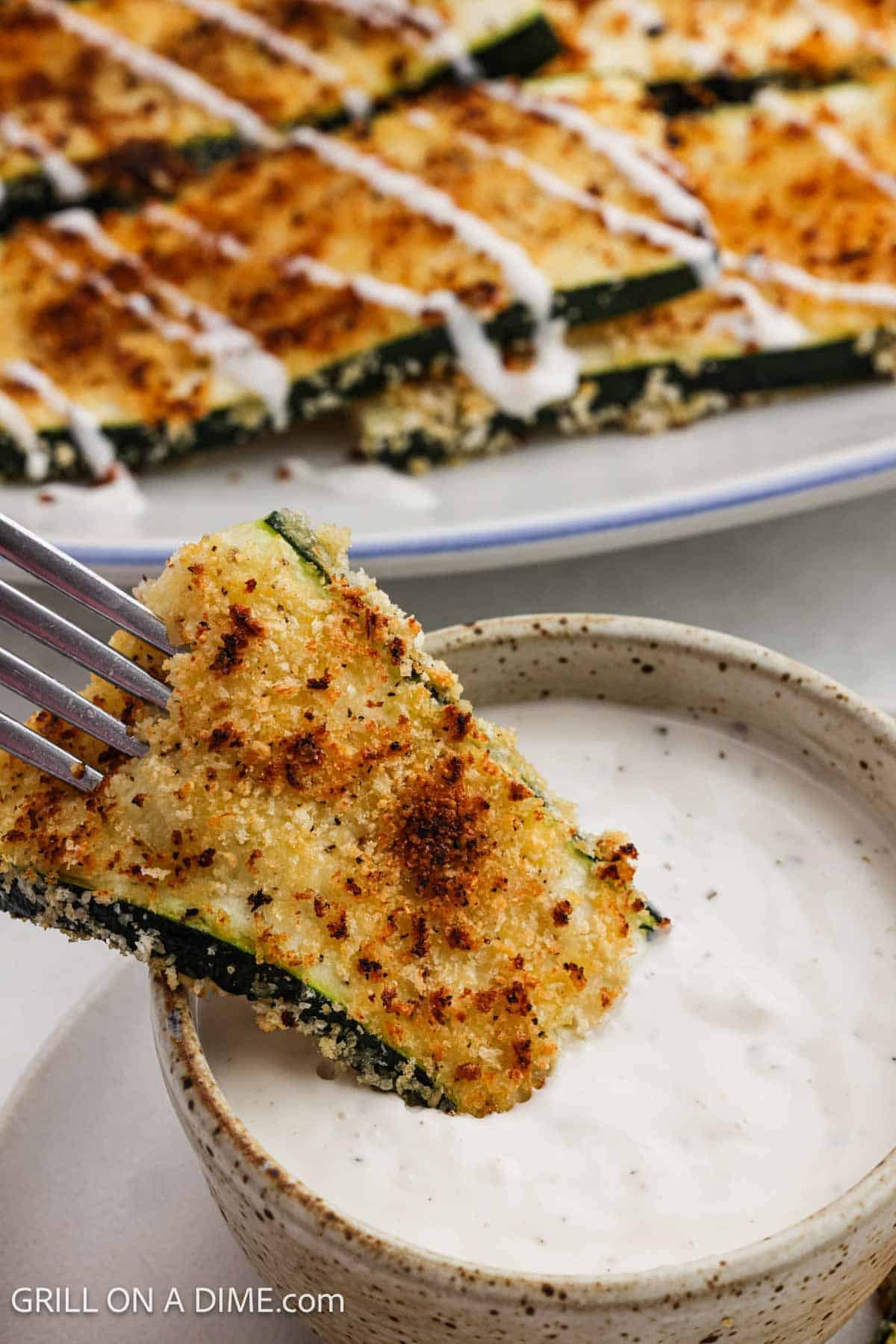 Dipping the golden brown coated zucchini in a bowl of ranch.