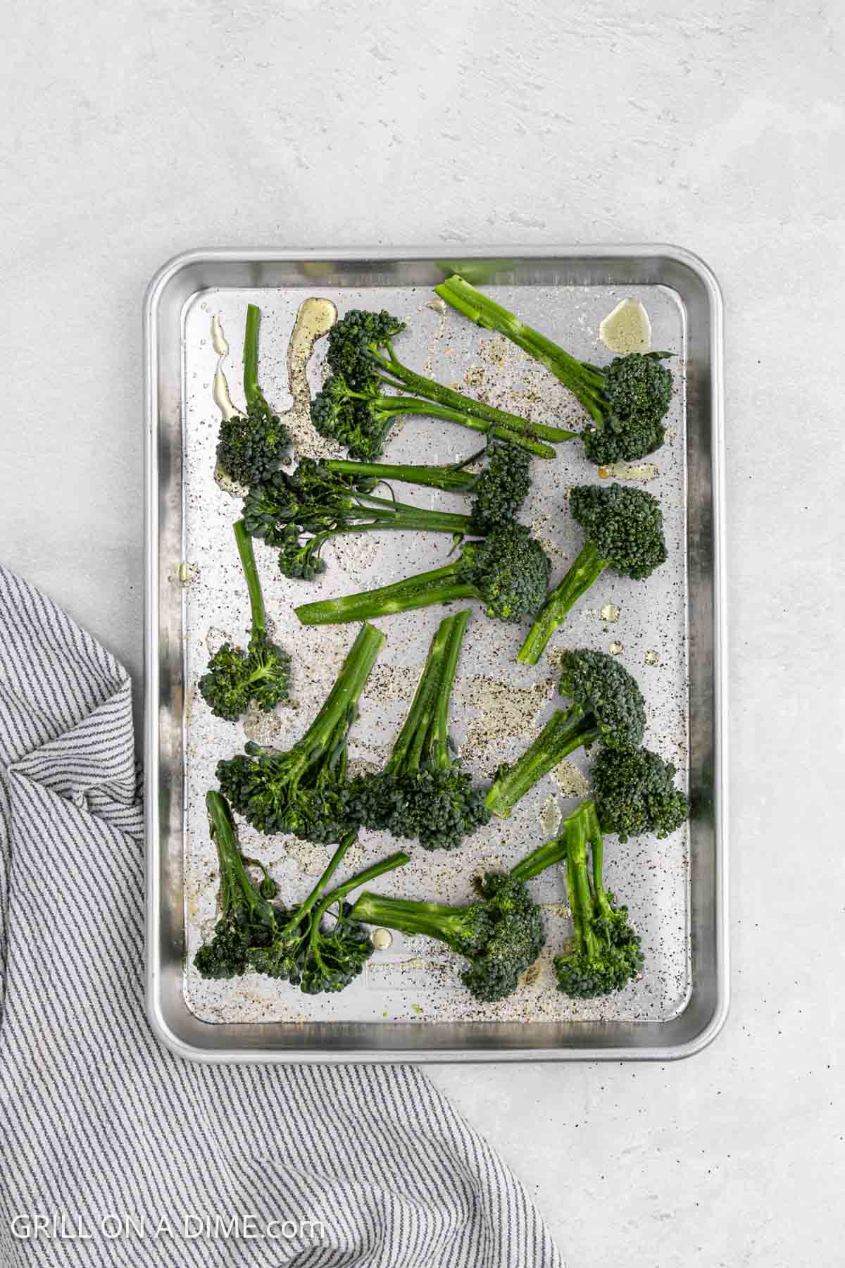Broccolini florets on a baking sheet topped with oil and salt and pepper. 