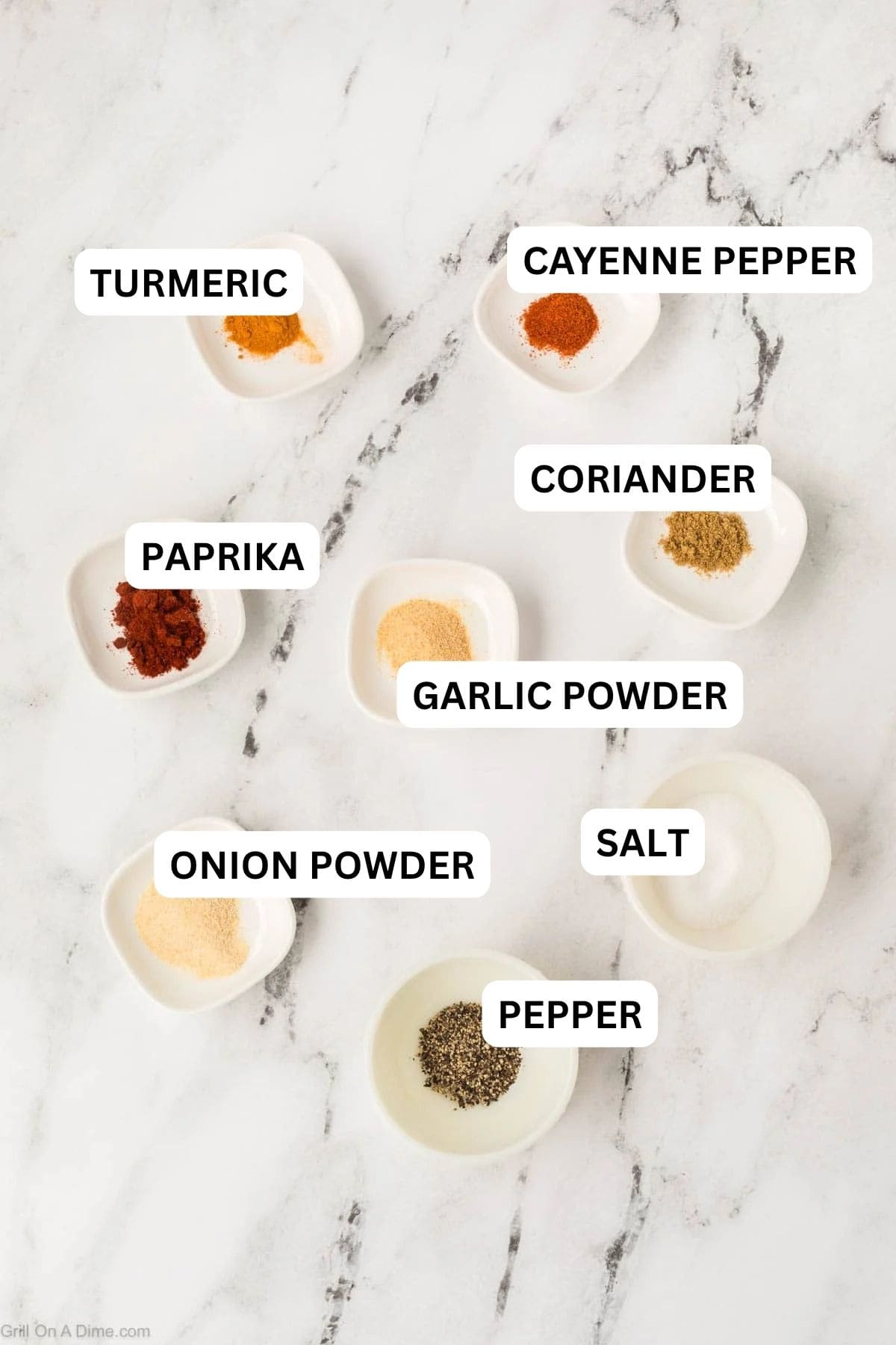 Eight small white bowls with different ground spices and seasonings to make this recipe. 