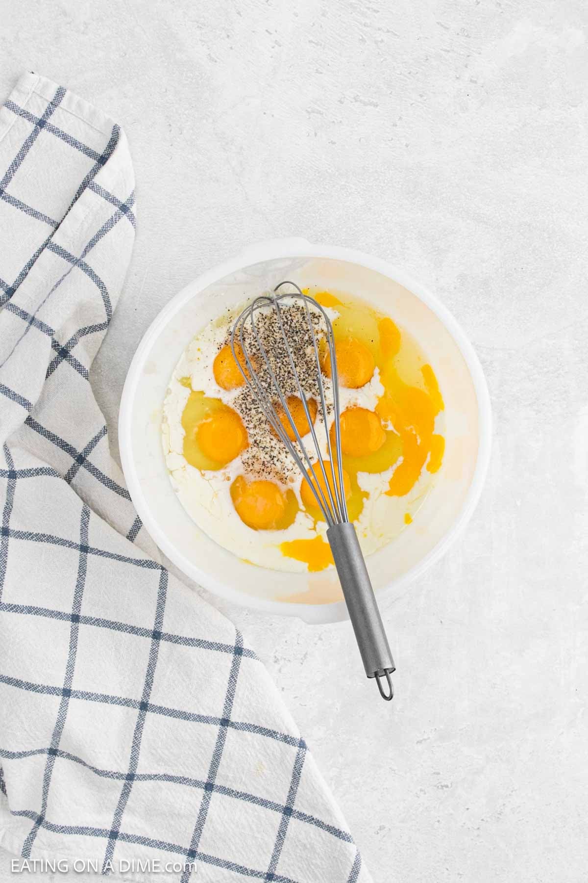 Mixing together milk, eggs and spices in a bowl with a whisk. 